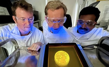 The nanoprobes engineered by (L-R) Dr Chris Howard, Professor Matt Trau, and Dr Selvakumar Edwardraja can be programmed to emit colourful or fluorescent reactions when they come into contact with a virus. three people in safety glasses and white coats look at a glowing round yellow dish on a metal table